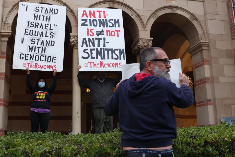 David Moritz holds a sign stating, "Anti-Zionism is Genocidal Anti-Semitism," in front of pro-Palestine protestors.