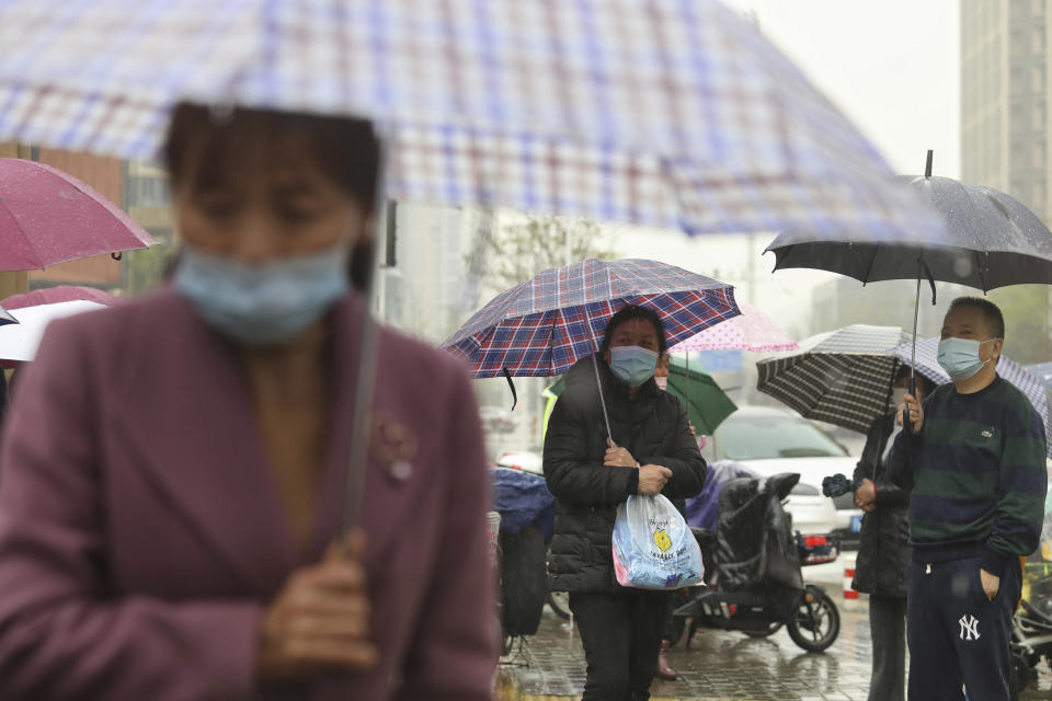 People wearing face masks to protect against COVID-19 wait in the rain to pick up children from a school in Wuhan in central China's Hubei Province, Friday, March 26, 2021. Chinese officials briefed diplomats Friday on the ongoing research into the origin of COVID-19, ahead of the expected release of a long-awaited report from the World Health Organization. (Chinatopix via AP)