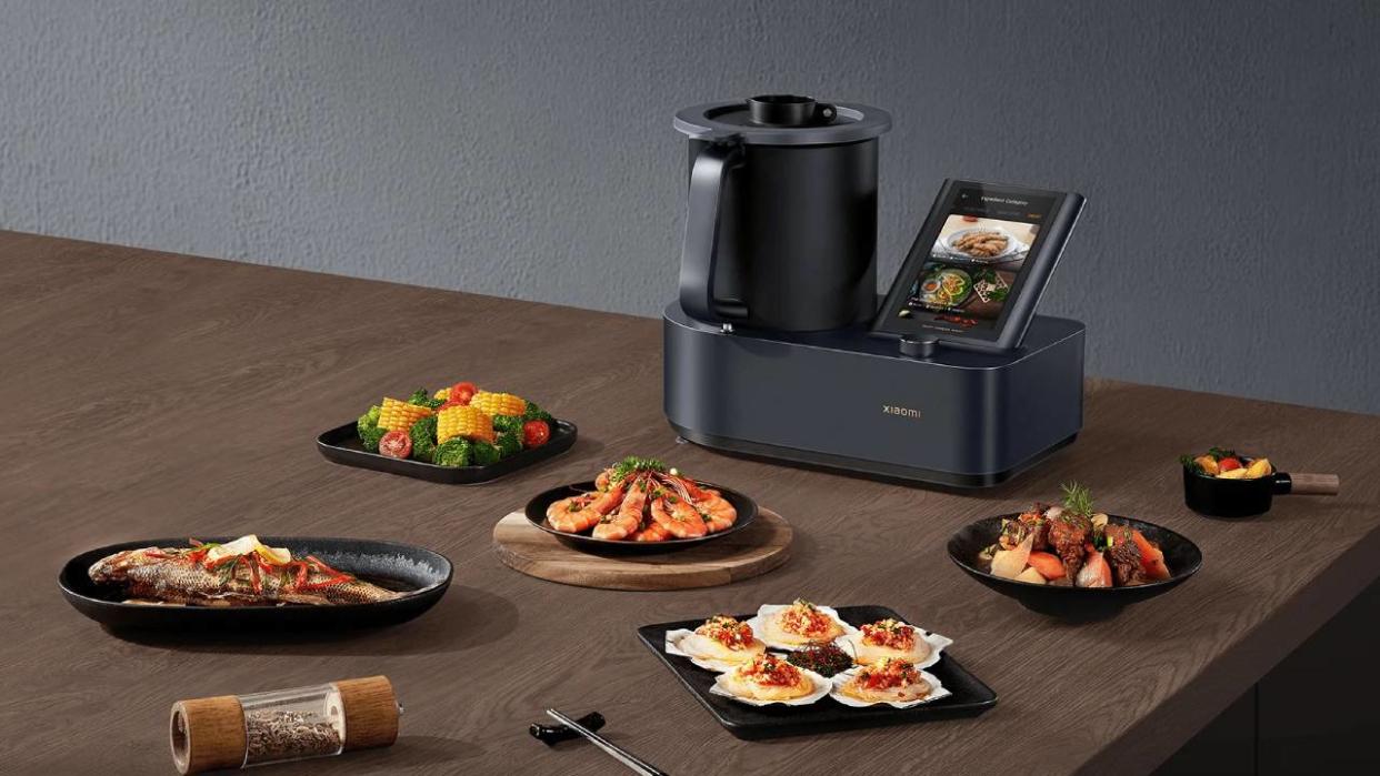  Lifestyle image of the Xiaomi Smart Cooking Robot surrounded by plates of food. 