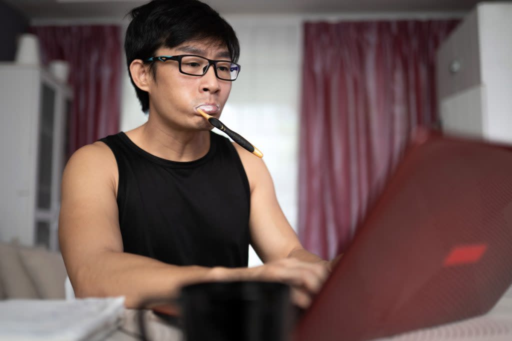 A man brushes his teeth while working from home. 