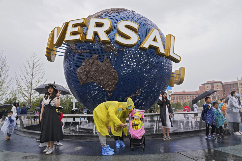 A family wearing raincoats and face masks to help protect themselves from the coronavirus pose for a selfie with an icon near the entrance to the Universal Studios Beijing in Beijing, Monday, Sept. 20, 2021. Thousands of people brave the rain visit to the newest location of the global brand of theme parks which officially opens on Monday. (AP Photo/Andy Wong)