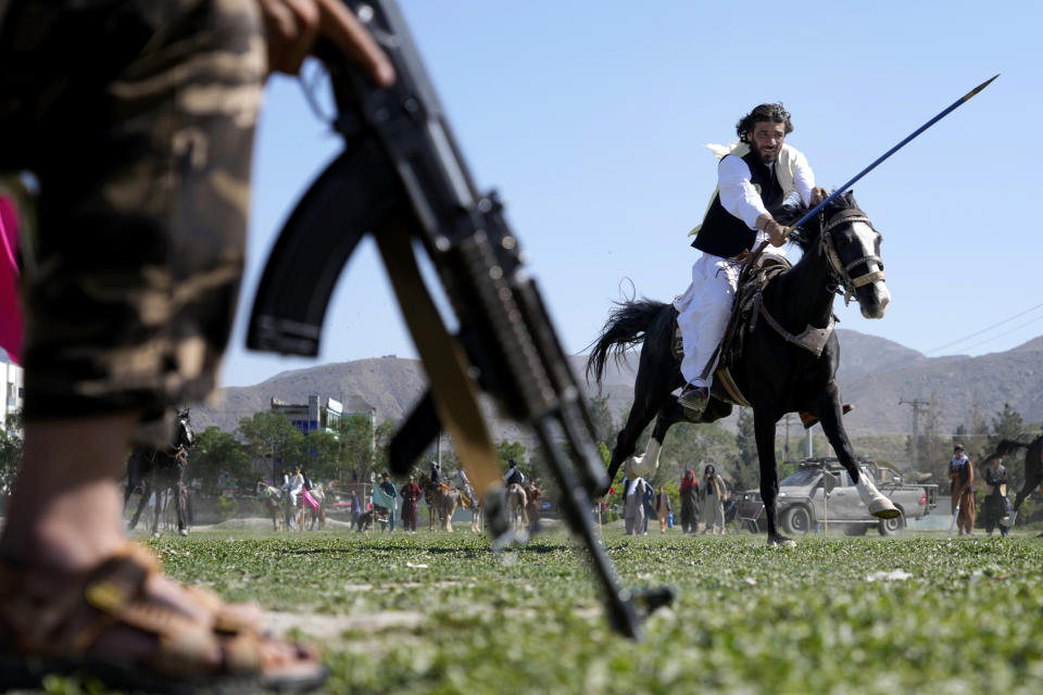 An Afghan man rushes to the target with his horse as a Taliban fighter stands guard during a spear racing in the sprawling Chaman-e-Huzori park in downtown Kabul, Afghanistan, Friday, May 6, 2022. (AP Photo/Ebrahim Noroozi)