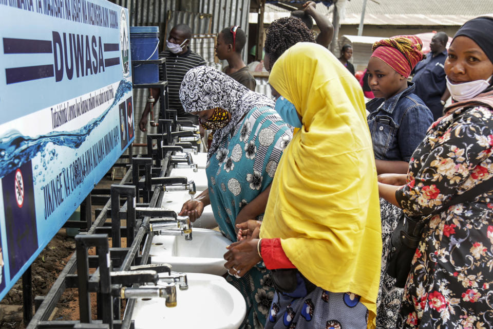 FILE - In this Monday, May 18, 2020 file photo, people use a hand-washing station installed for members of the public entering a market in Dodoma, Tanzania. Tanzania's president John Magufuli is finally acknowledging Sunday, Feb. 21, 2021 that his country has a coronavirus problem after claiming for months that the disease had been defeated by prayer, urging citizens to take precautions and even wear face masks - but only locally made ones. (AP Photo/File)