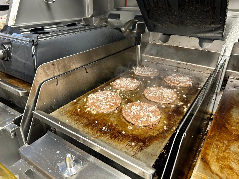 The image shows beef patties on the grill with diced white onions on top of them.