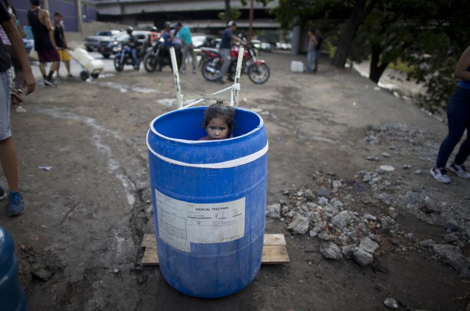 A little girl stands inside a plastic barrel while her family waits to collect water from an open pipe above the Guaire River, during rolling blackouts which affect the water pumps in people's homes, offices and stores, in Caracas, Venezuela, Monday, March 11, 2019. The blackout has intensified the toxic political climate, with opposition leader Juan Guaido blaming alleged government corruption and mismanagement and President Nicolas Maduro accusing his U.S.-backed adversary of sabotaging the national grid. (AP Photo/Ariana Cubillos)