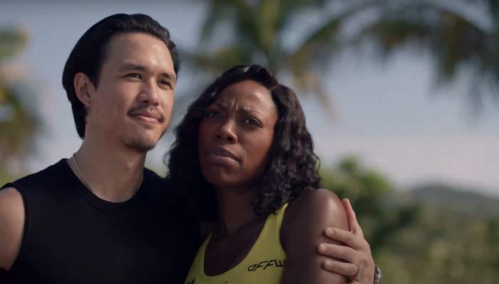 Charles Melton and Yvonne Orji stand closely together outdoors; Charles wears a black sleeveless shirt, and Yvonne wears a sleeveless yellow top