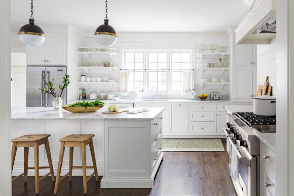 an all white farmhouse kitchen that has a big island and stainless steel appliances