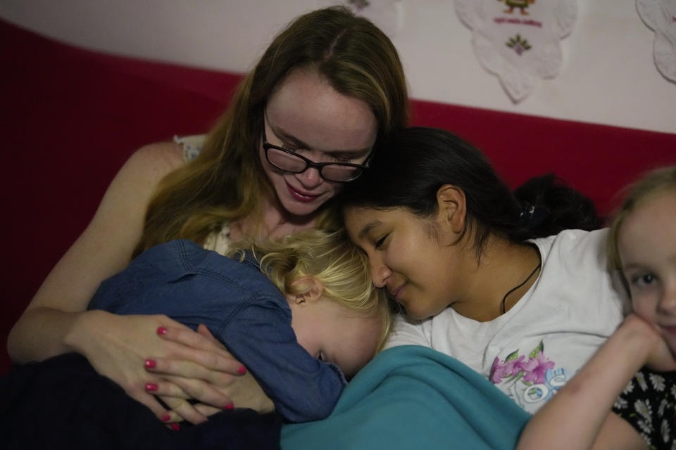 Sol, center, a 14-year-old from Argentina, snuggles up with her foster mother, Caroline Hazelton, and two of the Hazelton kids, Jessie, left, and Maddie, right, in Homestead, Fla., Monday, Dec. 18, 2023. Sol is among tens of thousands of children who have arrived in the United States without a parent during a huge surge in immigrants that's prompting congressional debate to change asylum laws. (AP Photo/Rebecca Blackwell)