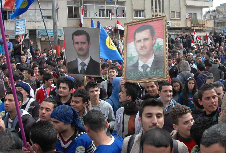 In this photo released by the Syrian official news agency SANA, supporters of Syrian President Bashar Assad, hold up his portraits as they march during a demonstration is solidarity with government forces, in al-Inshaat neighborhood of Homs, Syria, Wednesday Feb. 11, 2014. Meanwhile the Syrian government on Tuesday allowed over a hundred men of fighting age to leave rebel-held areas of the besieged city of Homs after they were questioned and cleared of rebel links, state media said. (AP Photo/SANA)