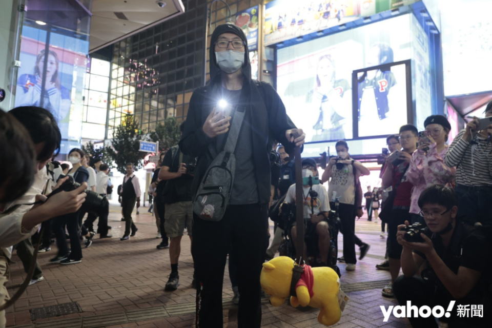 The man held a Winnie the Pooh doll on a leash in his left hand, and a mobile phone with a flash in his right hand.