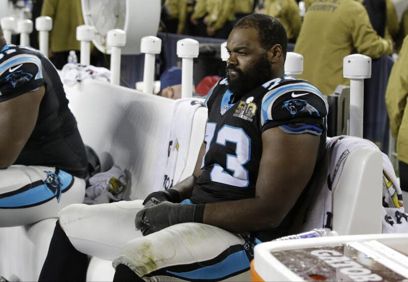 Michael Oher sitting on a bench in a black and light blue football uniform.