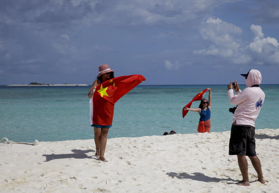 FILE - In this Sept. 14, 2014, file photo, Chinese tourists take souvenir photos with the Chinese national flag as they visit Quanfu Island, one of Paracel Islands of Sansha prefecture of southern China's Hainan province in the South China Sea. Vietnam's selection as the venue for the second summit between U.S. President Donald Trump and North Korean leader Kim Jong Un is largely a matter of convenience and security, but not without bigger stakes. Host Vietnam hopes to boost its international profile as diplomatic leverage against its big northern neighbor China, whose historical pushiness is manifested nowadays in its territorial claims in the South China Sea over waters claimed by Hanoi. (AP Photo/Peng Peng, File)