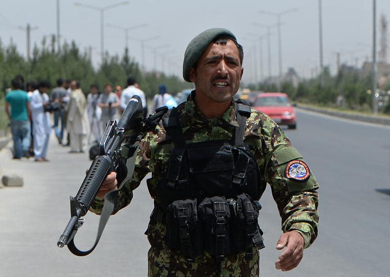 An Afghan soldier speaks to bystanders after a rocket attack by suspected Taliban militants on the military airport in Kabul, on July 3, 2014