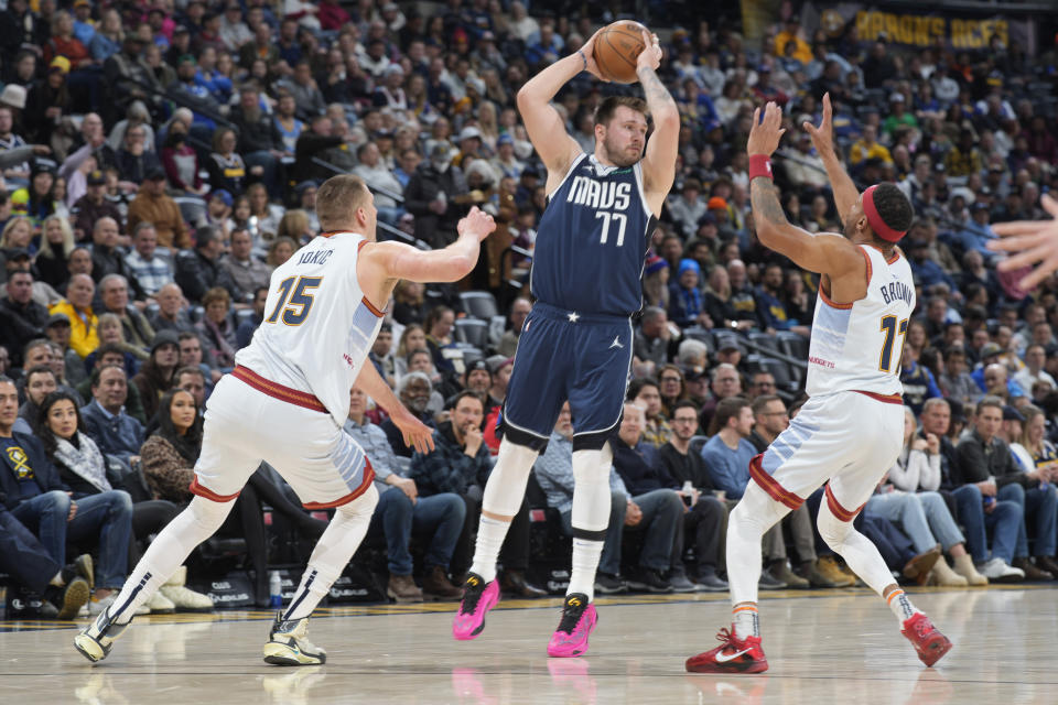 Dallas Mavericks guard Luka Doncic, center, looks to pass the ball as Denver Nuggets center Nikola Jokic, left, and forward Bruce Brown defend in the first half of an NBA basketball game Wednesday, Feb. 15, 2023, in Denver. (AP Photo/David Zalubowski)