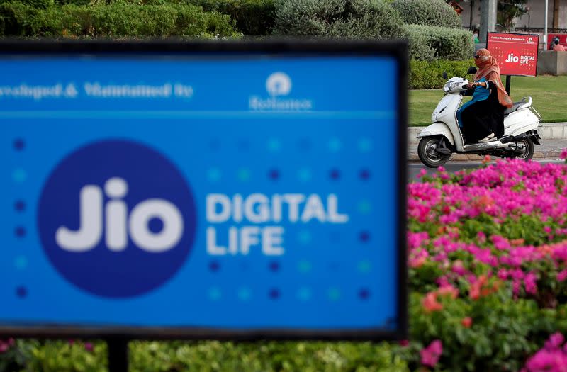 A woman rides her scooter past advertisements of Reliance Industries' Jio telecoms unit, in Ahmedabad