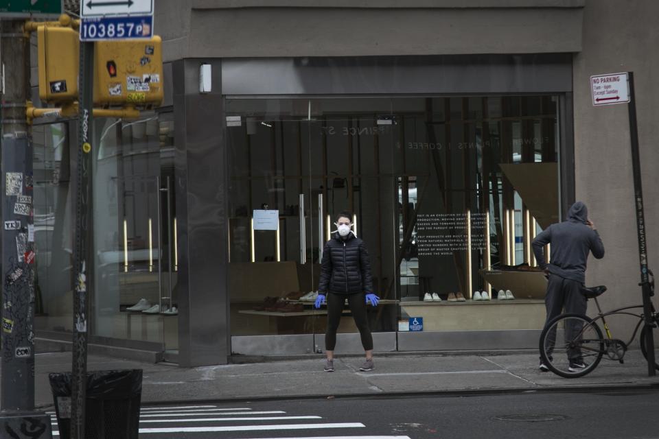 Una mujer con mascarilla y guantes quirúrgicos espera para cruzar la calle en Nueva York, el jueves 19 de marzo de 2020. (AP Foto/Wong Maye-E)