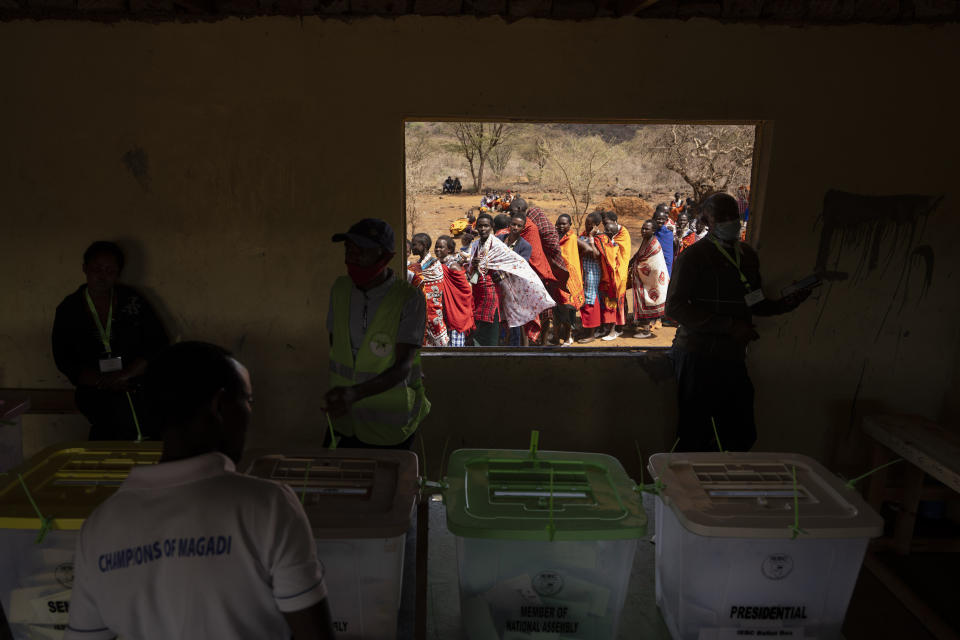 Votantes de la etnia masai, al fondo, hacen fila para sufragar mientras funcionarios electorales trabajan en el interior de una casilla de votación en la escuela primaria Niserian, en el condado de Kajiado, Kenia, el 9 de agosto de 2022. (AP Foto/Ben Curtis)