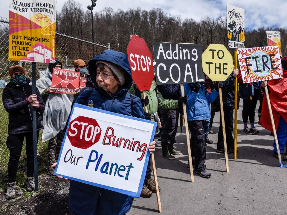 protestors wearing rain jackets hold signs saying stop burning our planet stop adding coal to the fire