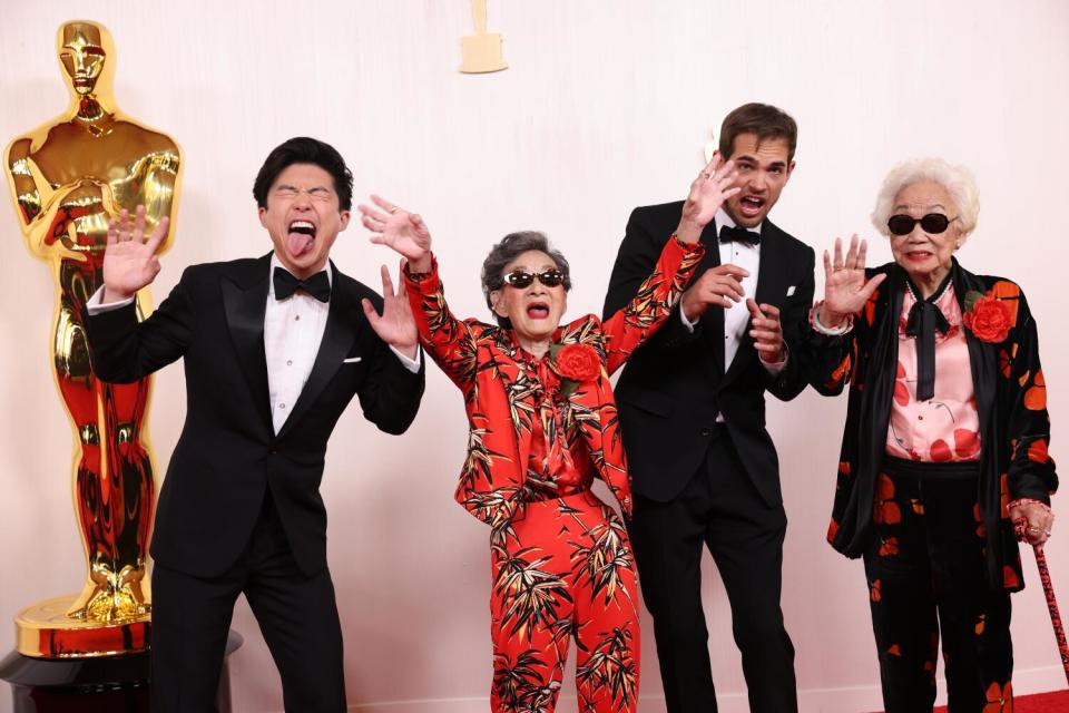 Two men and two older women in patterned suits wave.