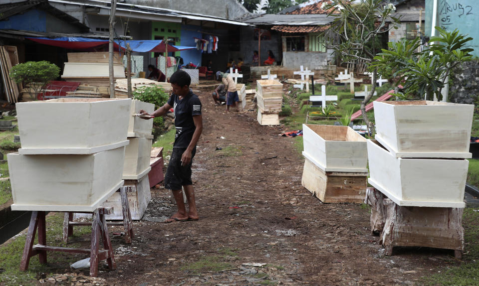 In this April 14, 2020, photo, a man paints a coffin prepared for victims of the new coronavirus in Jakarta, Indonesia. The world's fourth most populous nation now has the highest number of recorded fatalities from the COVID-19 disease in Asia after China, and testing for the viral infection remains among the lowest in the region. (AP Photo/Achmad Ibrahim)