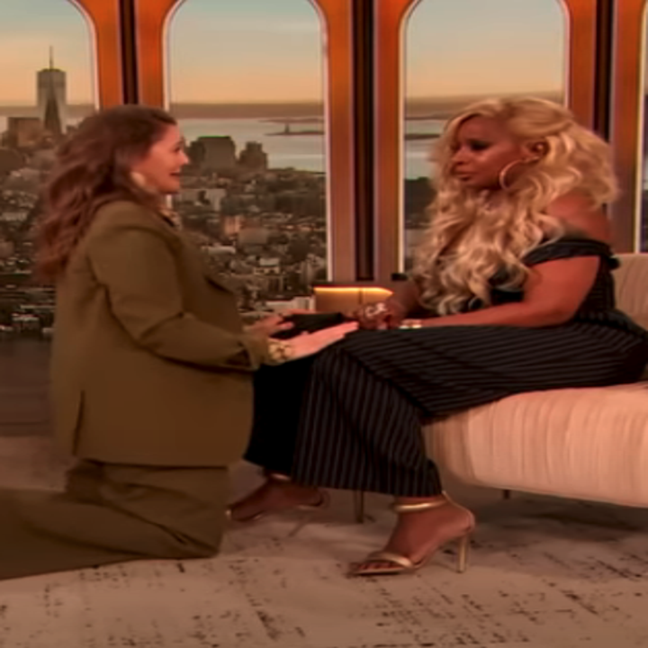 drew on her knees in a pantsuit in front of her talk show guest