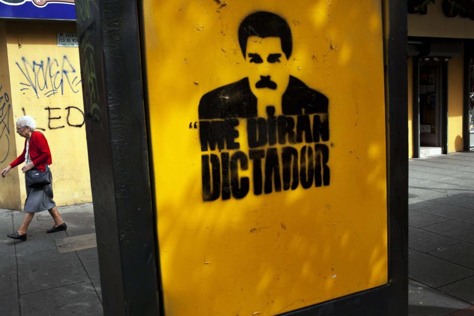 A woman walks next to a graffiti with the portrait of Venezuela's President Nicolas Maduro and a phrase that reads in Spanish:"They will call me dictator", downtown in Caracas, Venezuela, Thursday, Feb. 20, 2014. After a chaotic and tense night, with gunfire echoing through the streets of many neighborhoods, violence is heating up in Venezuela as an opposition leader faces criminal charges for organizing a rally that set off escalating turmoil in the oil-rich, but economically struggling country. (AP Photo/Rodrigo Abd)