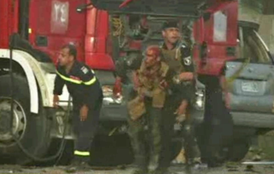 This image made from video shows a wounded Iraqi security forces member being assisted by a comrade after a series of bombs that exploded Friday, April 25, 2014 at a campaign rally for a Shiite group in Baghdad, Iraq, ahead of the country's parliamentary election. The blasts killed and wounded dozens, officials said. (AP Photo via AP video)