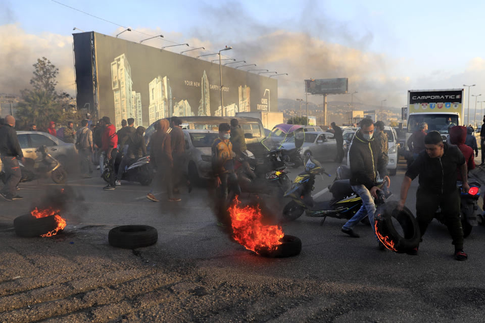 Protesters set burning tires on fire to block a highway that leads to Beirut's international airport, during a protest against against the economic and financial crisis, in Beirut, Lebanon, Tuesday, March 2, 2021. The Lebanese pound has hit a record low against the dollar on the black market as the country's political crisis deepens and foreign currency reserves dwindle further. (AP Photo/Hussein Malla)