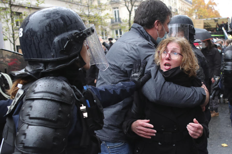 A riot police officer pushes a couple during a protest, Saturday, Dec.12, 2020 in Paris. Protests are planned in France against a proposed bill that could make it more difficult for witnesses to film police officers. (AP Photo/Thibault Camus)