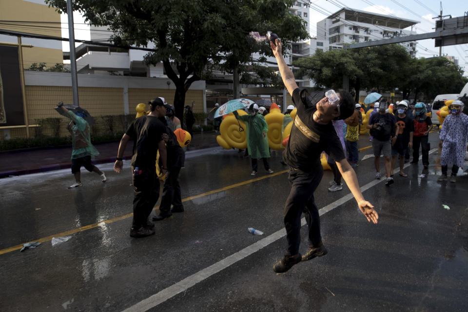 A pro-democracy protester hurls a color paint ball as police fire water cannons during an anti-government rally near the Parliament in Bangkok, Tuesday, Nov. 17, 2020. Thailand's political battleground shifted to the country's Parliament Tuesday, where lawmakers are considering proposals to amend the country's constitution, one of the core demands of the student-led pro-democracy movement. (AP Photo/Wason Wanichakorn)