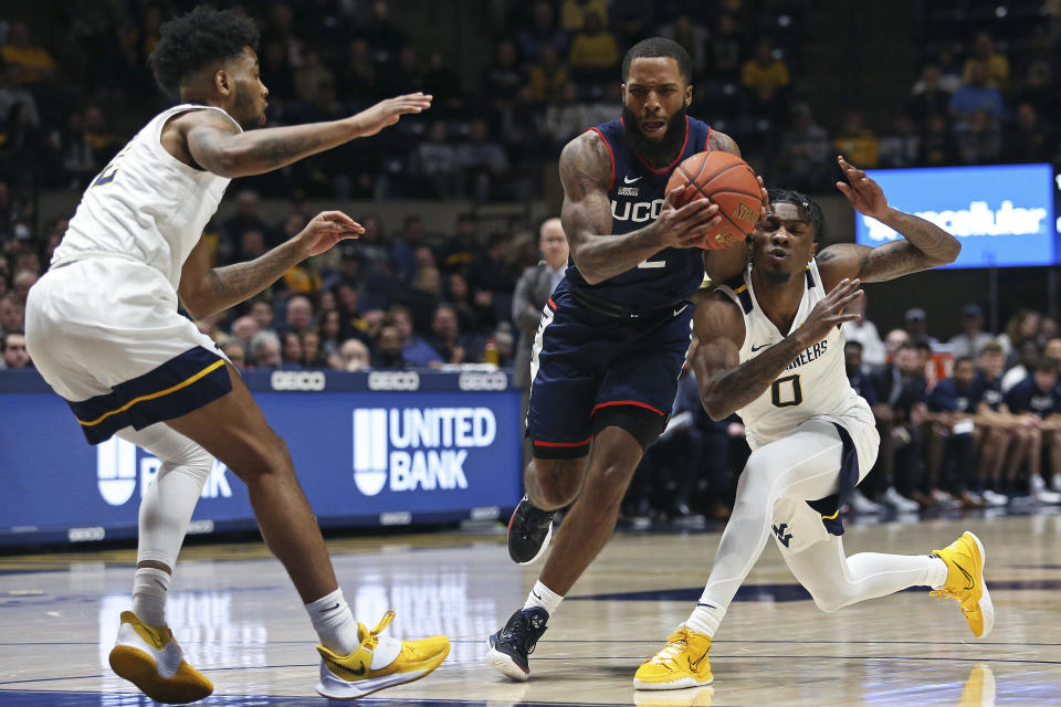 Connecticut guard R.J. Cole, center, is defended by West Virginia guards Taz Sherman, left, and Kedrian Johnson (0) during the first half of an NCAA college basketball game in Morgantown, W.Va., Wednesday, Dec. 8, 2021. (AP Photo/Kathleen Batten)
