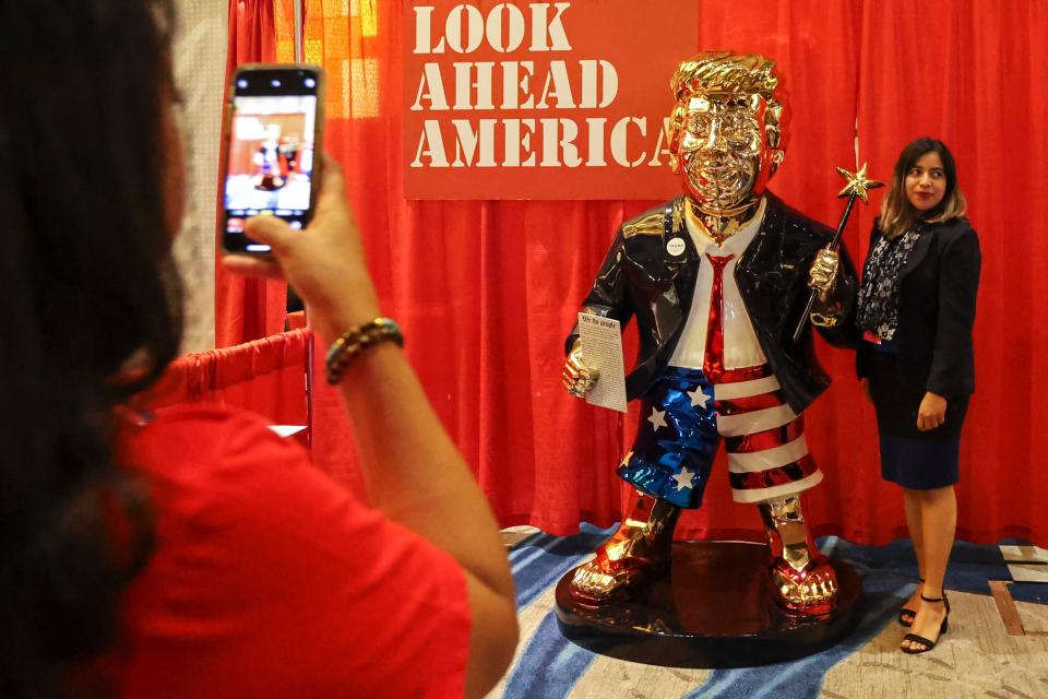 A woman takes a photo with a golden Donald Trump statue at the Conservative Political Action (CPAC) conference on Friday, Feb. 26, 2021, in Orlando, Fla. (Sam Thomas/Orlando Sentinel via AP) ORG XMIT: FLORL801