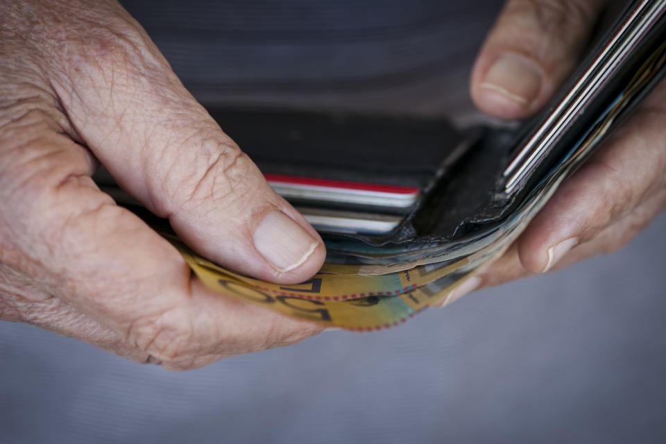 Close-up of a man&#39;s hands removing Australian notes from a wallet with gift cards