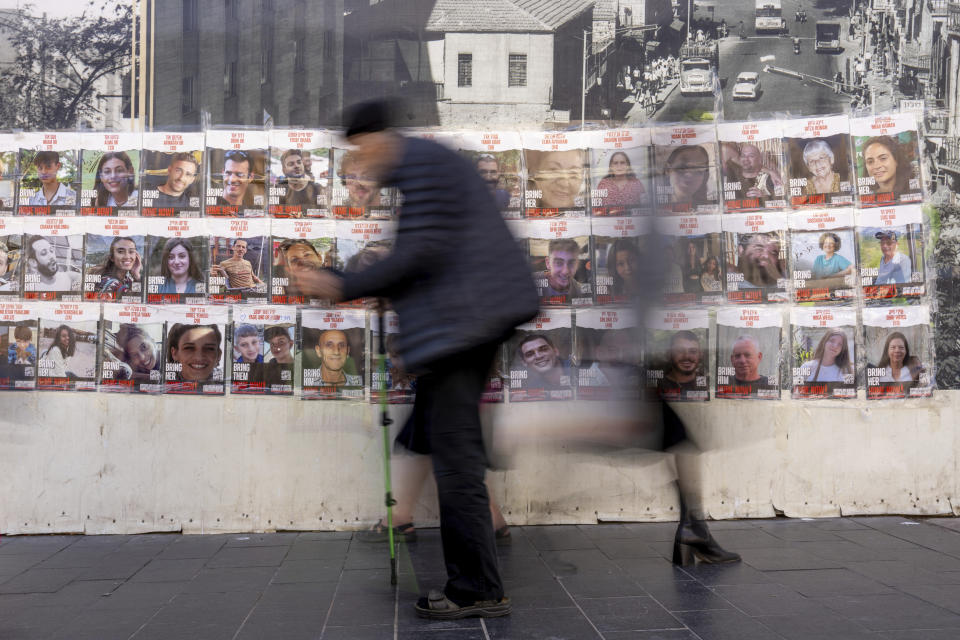 People walk past a wall with photos of the hostages who are believed to remain captive in the Gaza Strip, in Jerusalem, Sunday, Dec. 3, 2023. (AP Photo/Ohad Zwigenberg)