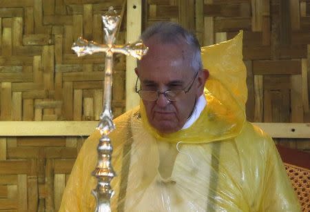Pope Francis, in a rain poncho, attends during a Mass near Tacloban airport January 17, 2015. REUTERS/ Stefano Rellandini
