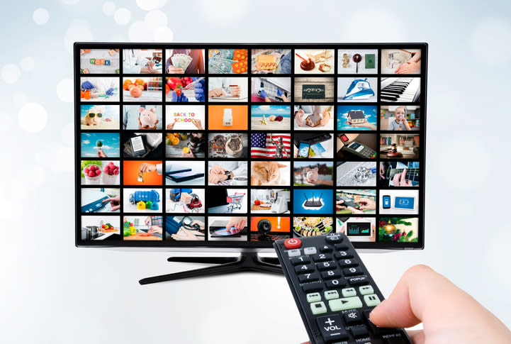 Hand holding a TV remote control pointing at a digital TV with many images/channels shown on menu.