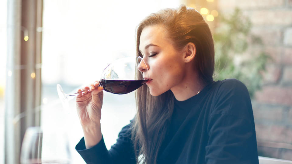 Beautiful young woman drinking red wine with friends in cafe, portrait with wine glass near window.