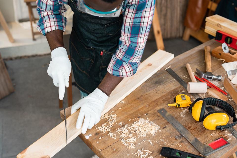 man cutting through block of wood using saw, close up of hands