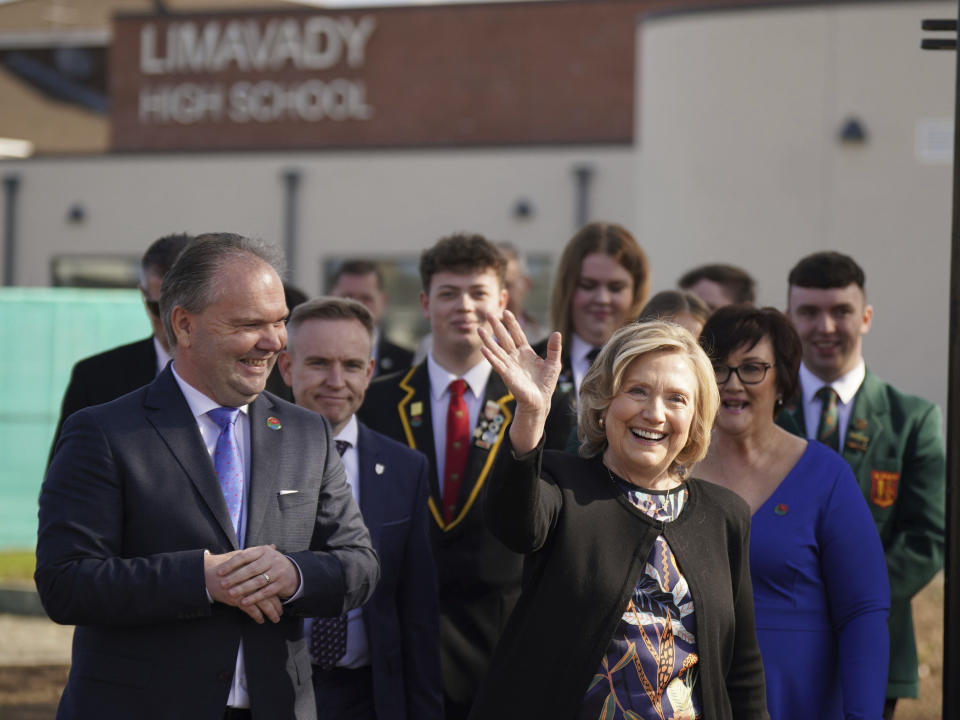 Former US secretary of state and Chancellor of Queen's University Belfast, Hillary Clinton waves as she walks with Darren Mornin, left, principal of Limavady High School and Rita Moore, right, principal of the adjacent St Mary's High School during a visit to Limavady High School, Co Londonderry, Northern Ireland, to preside over an honorary graduation ceremony, marking the contribution of Principals from St Mary's High School and Limavady High School in the development of the Shared Education model, Wednesday April 19, 2023. (Niall Carson/PA via AP)
