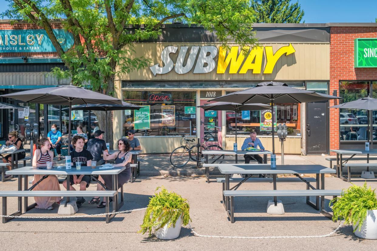 People eat outdoors on a Subway fast-food restaurant patio in Hamilton, Ontario, Canada on a sunny day.