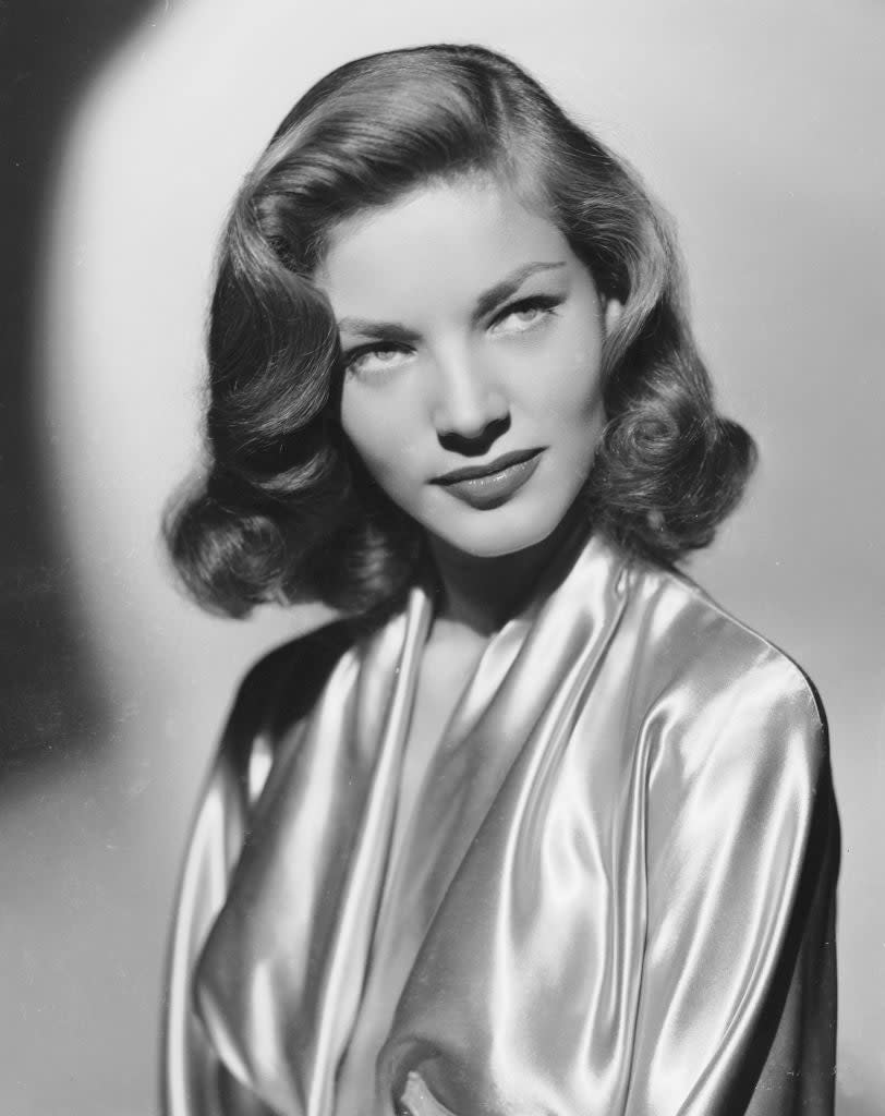 Lauren Bacall in a classic Hollywood portrait, wearing a satin robe and looking slightly off-camera with vintage curled hair