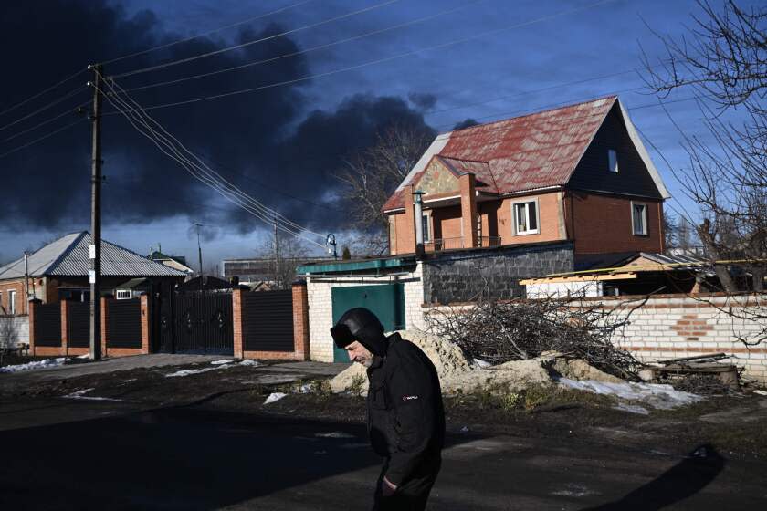 A man walks in a street as black smoke rises from a military airport in Chuguyev near Kharkiv on February 24, 2022. - Russian President Vladimir Putin announced a military operation in Ukraine today with explosions heard soon after across the country and its foreign minister warning a "full-scale invasion" was underway. (Photo by Aris Messinis / AFP) (Photo by ARIS MESSINIS/AFP via Getty Images)