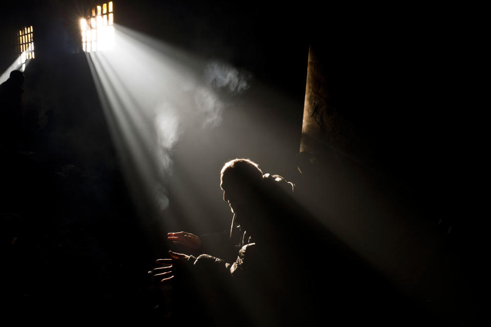 <p>FEB. 4, 2017 – A migrant from Pakistan warms himself around a fire in an abandoned warehouse where he and other migrants took refuge in Belgrade, Serbia. Hundreds of migrants have been sleeping rough in freezing conditions in central Belgrade looking for ways to cross the heavily guarded EU borders. (Photo: Muhammed Muheisen/AP) </p>