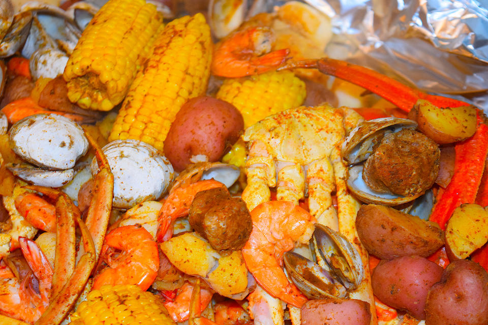 A steaming seafood boil featuring crab legs, shrimp, clams, corn on the cob, and potatoes arranged appetizingly