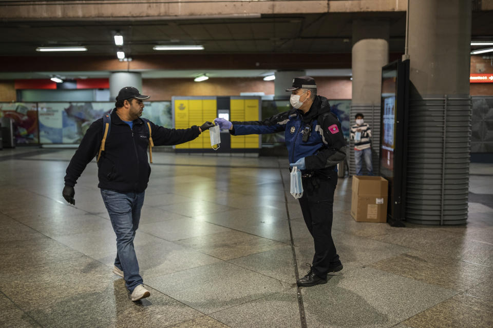 A local police distributes face masks to commuters at Atocha train station during the coronavirus outbreak in Madrid, Spain, Monday, April 13, 2020. Confronting both a public health emergency and long-term economic injury, Spain is cautiously re-starting some business activity to emerge from the nationwide near-total freeze that helped slow the country's grim coronavirus outbreak. The new coronavirus causes mild or moderate symptoms for most people, but for some, especially older adults and people with existing health problems, it can cause more severe illness or death. (AP Photo/Bernat Armangue)