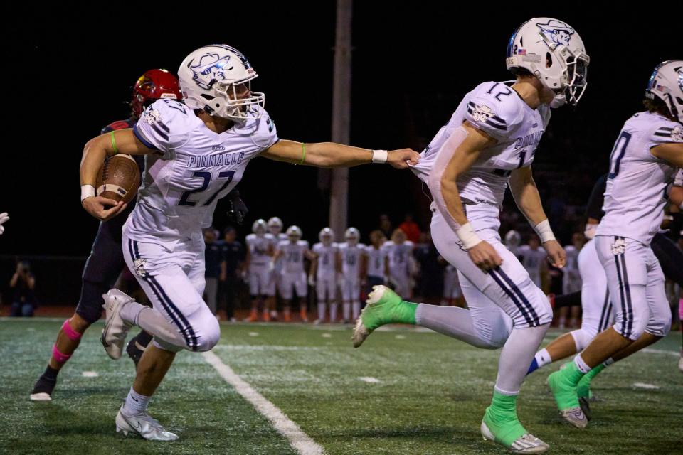 Pinnacle Pioneers junior running back Mason O'Rourke (27) grabs the back of his teammate junior linebacker Spencer Halvorson (12) as he drives the ball upfield at Chaparral High School's football field in Scottsdale on Oct. 14, 2022.