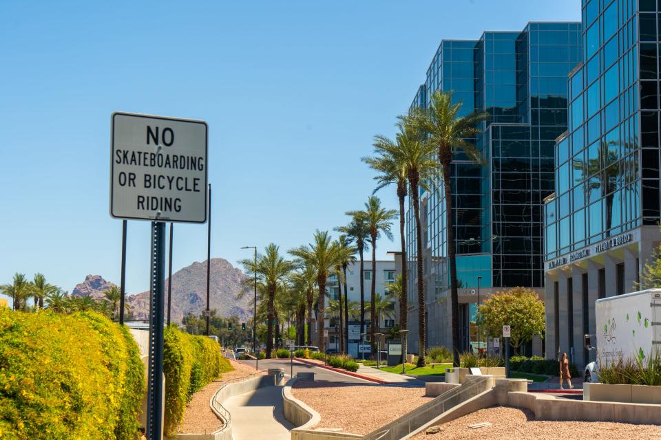 A curvy street in Scottsdale lined with modern buildings and palm trees. Mountains and blue skies in the background