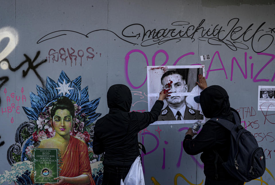 Demonstrators paste a portrait of National Police Chief Mario Rozas on the wall before painting it red to symbolize police brutality during a march against the commemoration of the discovery of the Americas, organized by Indigenous groups demanding autonomy and the recovery of ancestral land in Santiago, Chile, Monday, Oct. 12, 2020. (AP Photo/Esteban Felix)