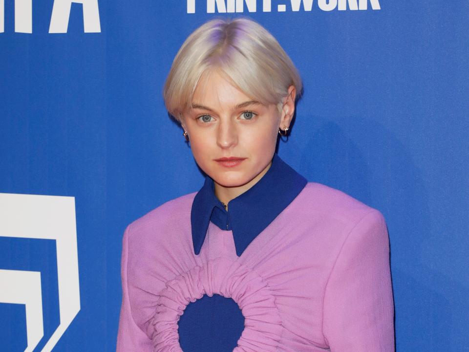 Emma posing in short blonde hair and a blue and pink blouse.