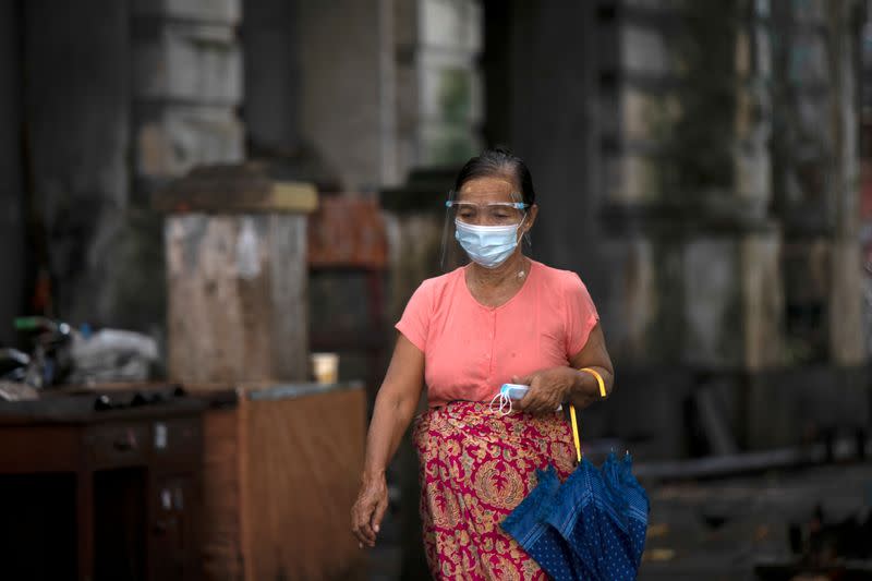 Woman with a face shield, holding extra masks, walks down the street in Yangon